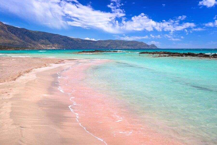 Idyllic tropical beach with pink sand, turquoise waters, and lush mountainous backdrop.