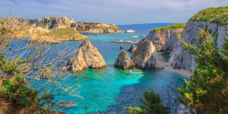 Stunning coastal bay, cliffs, turquoise water, boats; serene landscape with historic structure.