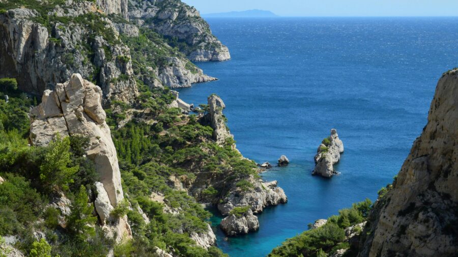 Stunning coastal cliffs with lush greenery, turquoise waters, and clear blue sky on a sunny day.
