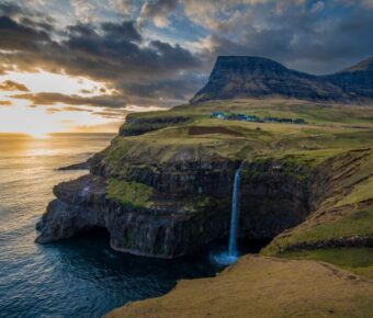 Majestic coastal waterfall with rugged cliffs and mountain, Faroe Islands scenic beauty.