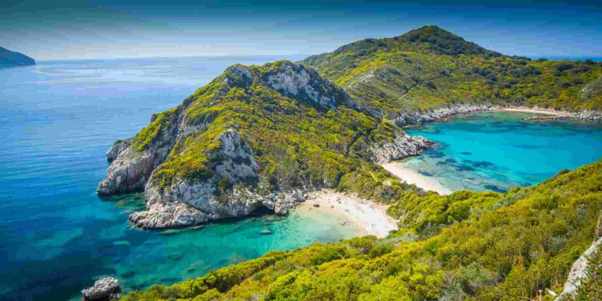 Stunning coastal landscape with lush greenery, rocky outcrop, clear waters, and serene beach.