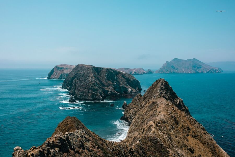 Rugged coastal cliffs and islands under clear sky with turquoise ocean water.