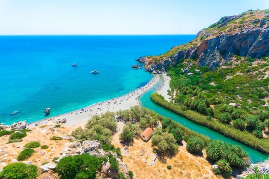 Mediterranean coastal scene with vibrant blue sea, sandy beach, boats, and lush greenery.