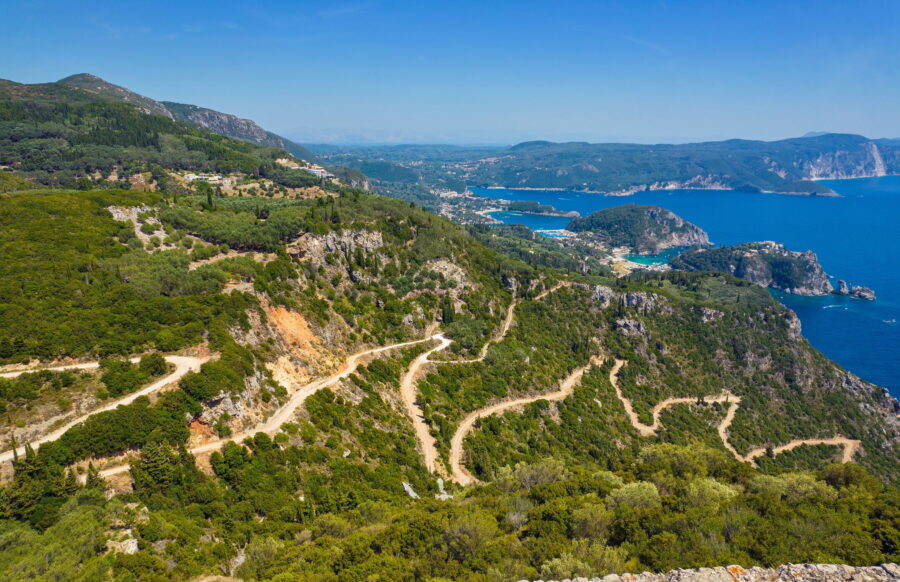Stunning mountainous coastal view with lush greenery, turquoise sea, trails, and developed beachfront.