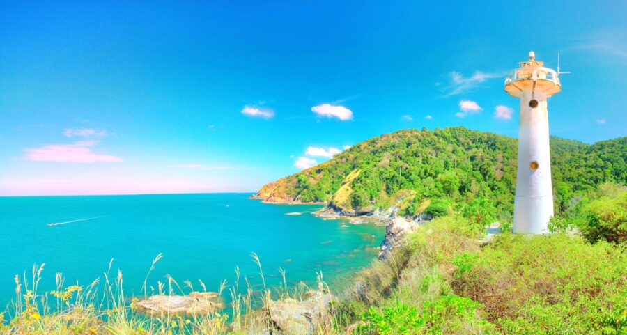 Scenic coastal lighthouse overlooking turquoise ocean bay, green cliffs, blue sky, tranquil seascape view.