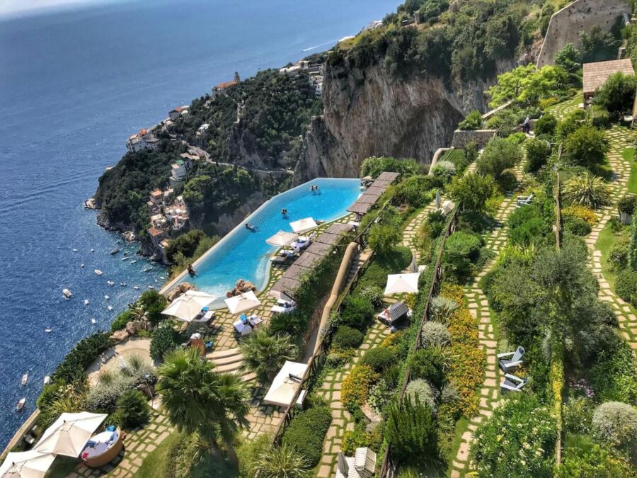 Luxurious hillside resort overlooking the ocean with infinity pool, lush gardens, and cliffs.