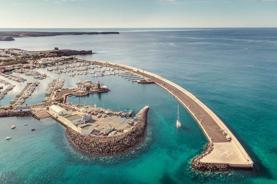 Aerial view of Marina Rubicón harbor, boats, breakwater and turquoise Atlantic Ocean coastline.