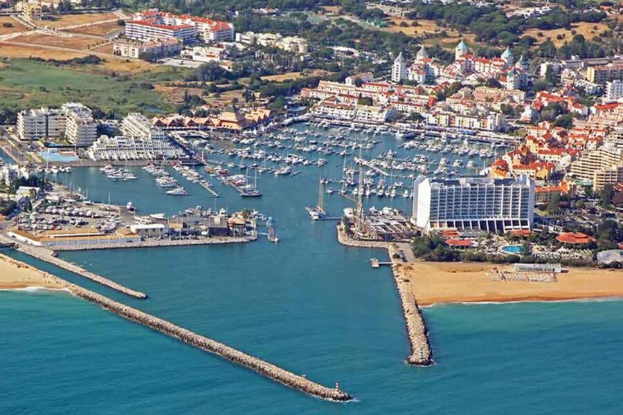 Aerial view of a vibrant Vilamoura marina with boats, modern architecture, and scenic beach.