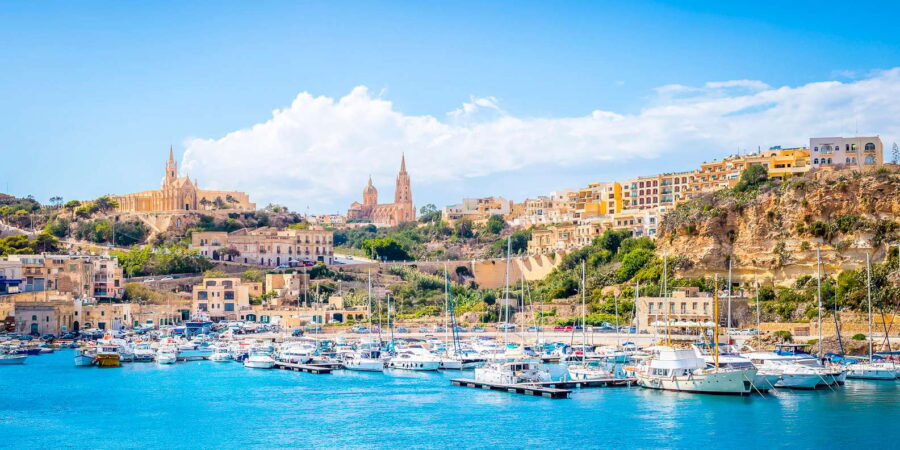 Gozo, Malta marina and harbor panorama with boats, turquoise sea, and historic coastal town.