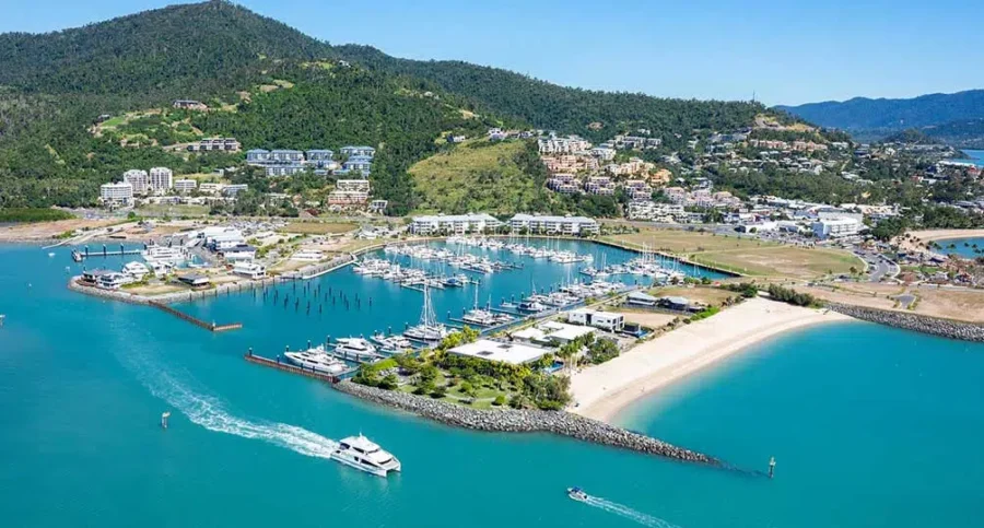 Airlie Beach marina and resort town with yachts, turquoise bay, tropical hills and waterfront hotels.