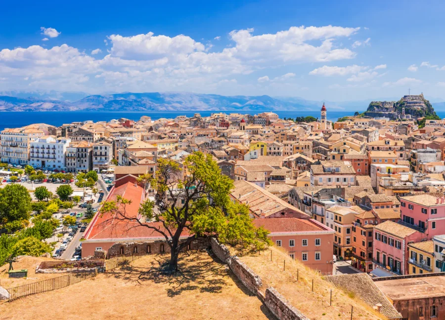 Panoramic coastal Mediterranean town with terracotta rooftops, historic buildings, and sea view.