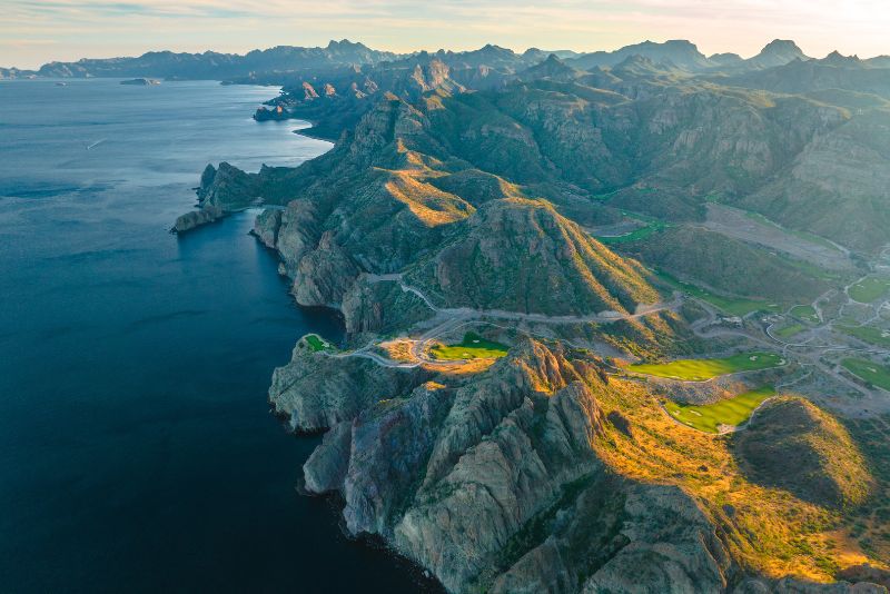Aerial view of Baja coastal mountains, desert cliffs and oceanfront golf course along rugged shoreline.
