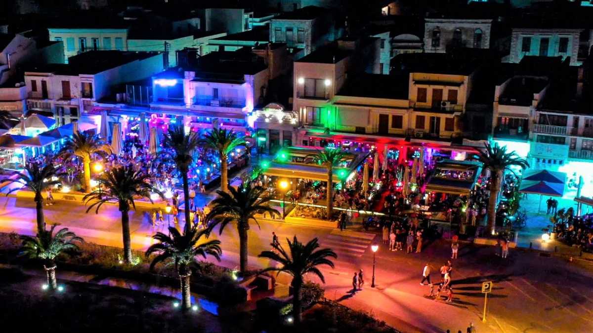 Vibrant coastal nightlife: palm trees, colorful lights, festive gatherings, lively architecture.
