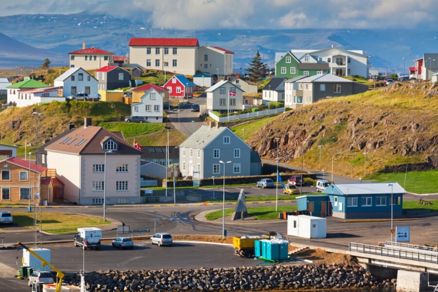 Picturesque coastal Nordic town with colorful hillside houses, ocean views, and mountain backdrop.