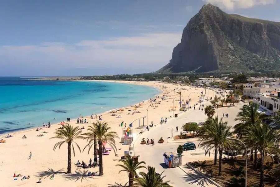 Beachfront oasis in San Vito Lo Capo with sunbathers, turquoise waters, and mountain backdrop.