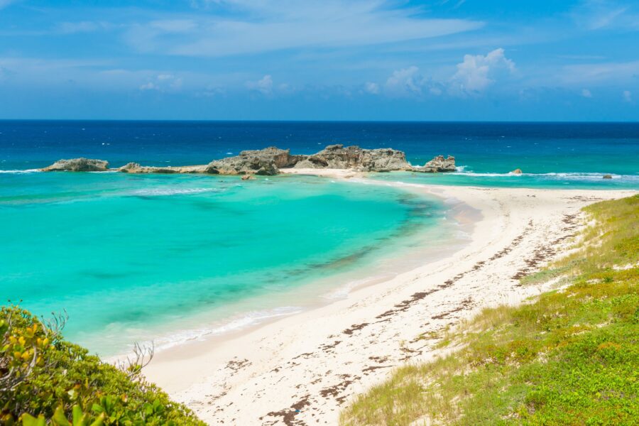 Idyllic Caribbean beach with turquoise waves, rocky outcrops, and lush shoreline vegetation.