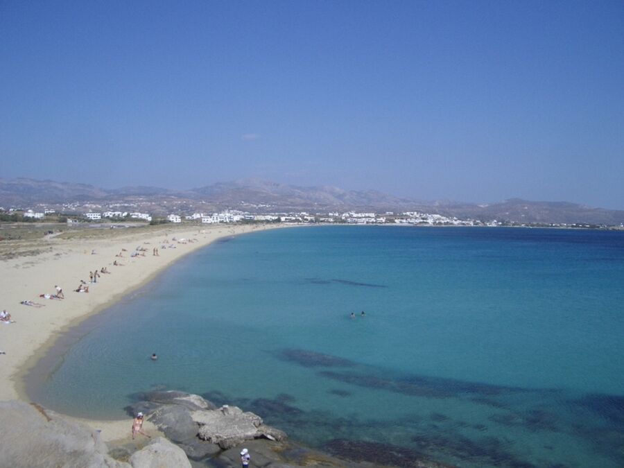 Idyllic beach scene with azure waters, whitewashed buildings, and sunbathing beachgoers in Greece.