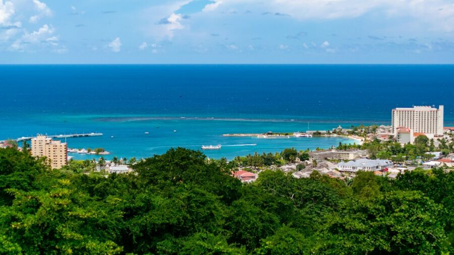 Caribbean coastal view with vibrant sea, lush greenery, boats, urban development, and clear skies.