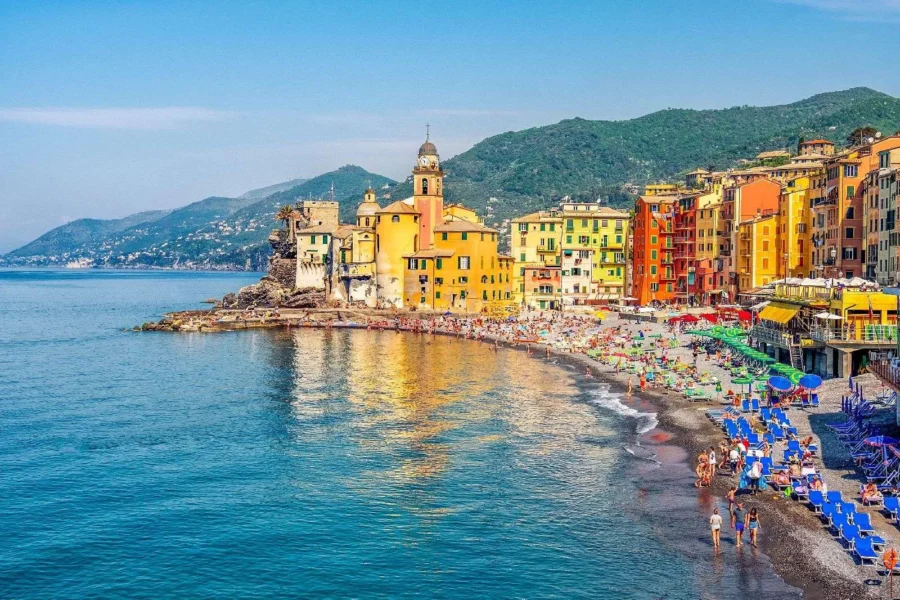 Camogli seaside town with pastel houses, pebble beach, church tower and aquamarine Ligurian sea.