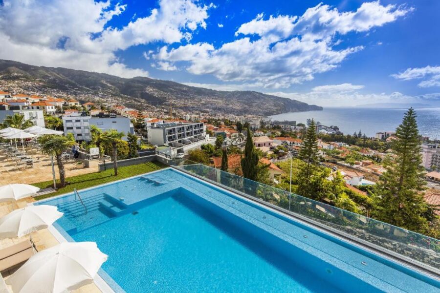 Madeira coastal hotel pool terrace with sea, hillside town, and mountain views.