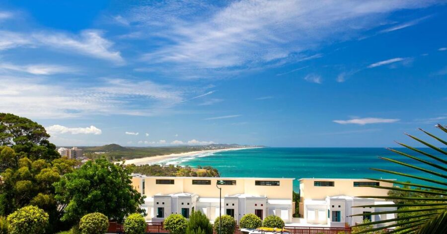 Aerial view of Coolum beachfront resort, golden sand beach, turquoise ocean and lush tropical greenery.