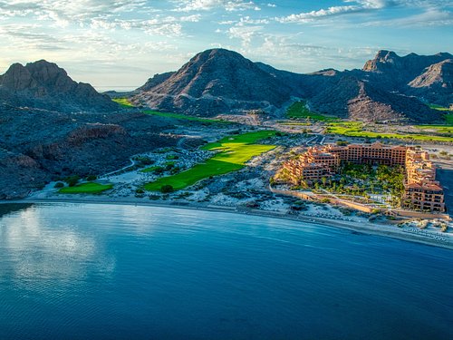 Luxury coastal resort with golf course beside calm ocean and desert mountains in Mexico.