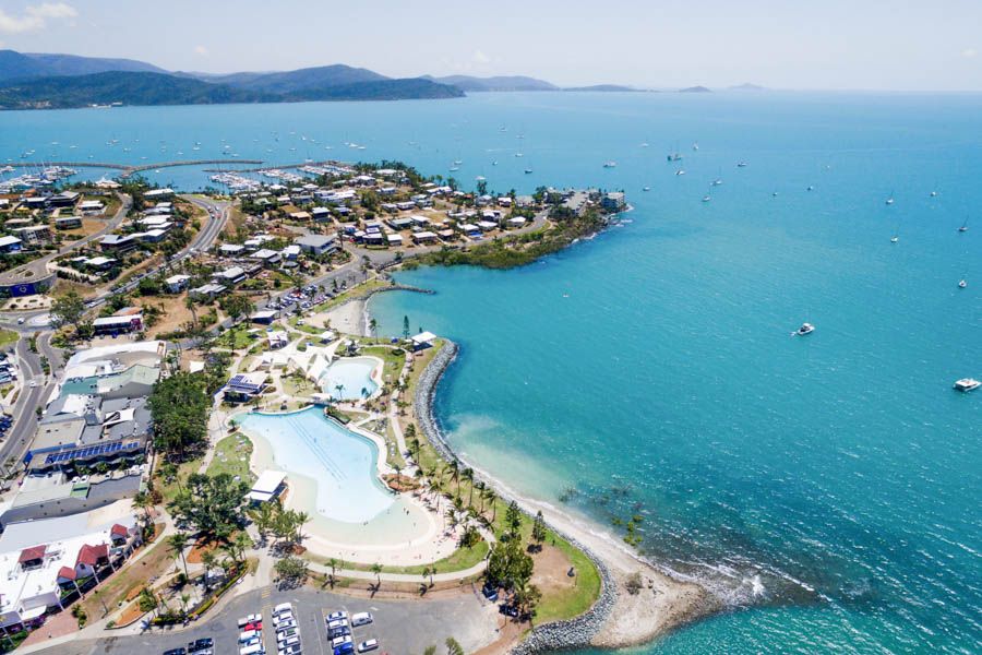 Aerial view of Airlie Beach coastal resort lagoon, sandy bay, turquoise ocean and boats.