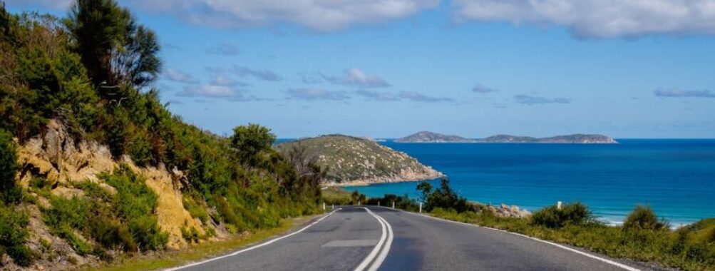 Scenic US East Coast road with lush greenery, ocean views, and clear blue skies.