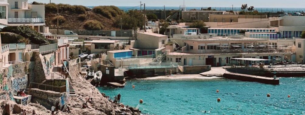 Picturesque coastal scene with turquoise waters, rocky outcrops, colorful buildings, and vibrant graffiti.