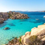 Picturesque coastal scene with turquoise waters, rocky outcrops, colorful buildings, and vibrant graffiti.