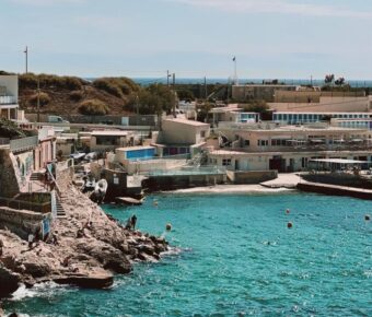 Picturesque coastal scene with turquoise waters, rocky outcrops, colorful buildings, and vibrant graffiti.