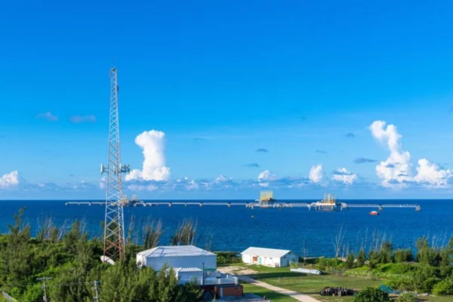 Coastal landscape with communications tower, ocean, greenery, and offshore platforms.