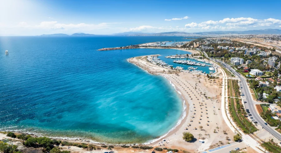 Aerial view of Glyfada Beach: turquoise sea, sandy shoreline, marina, and palm trees.