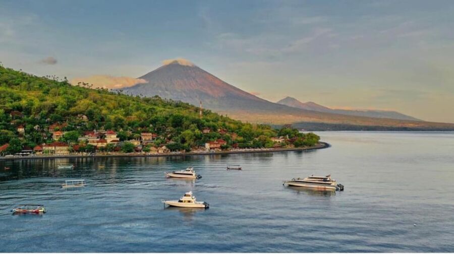 Amed  Scenic coastal village with boats and volcano backdrop in serene, tropical setting.