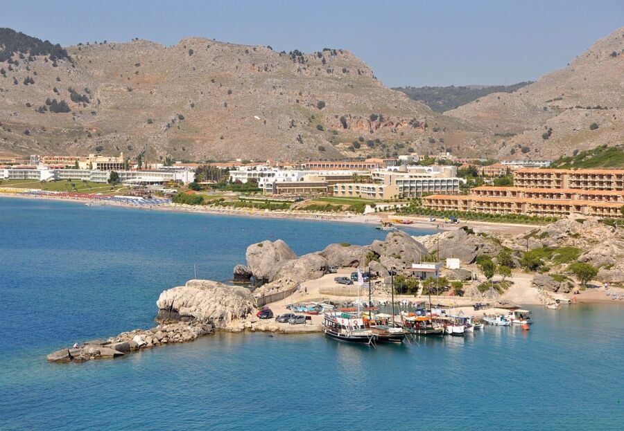 Scenic coastal bay with turquoise waters, sandy beaches, boats, mountain views, and vibrant resorts.