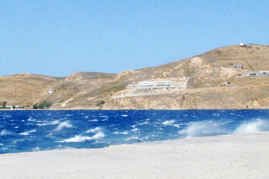 Coastal scene with vibrant sea, sandy shoreline, rugged hills, and modern hillside structure.