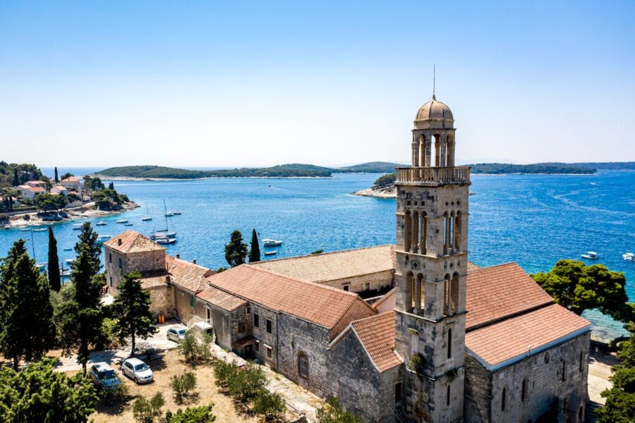 Historic coastal church with bell tower, lush garden, sea view, and Mediterranean setting.
