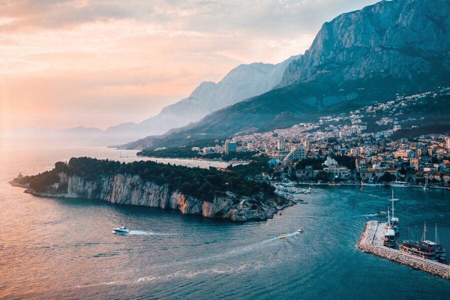 Coastal sunset, tranquil sea, dramatic mountains, vibrant town, and peaceful evening scene.