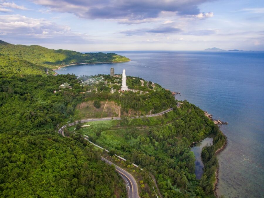 Aerial view of Son Tra Peninsula coastal temple complex, Buddhist statue, lush green hills, and sea.