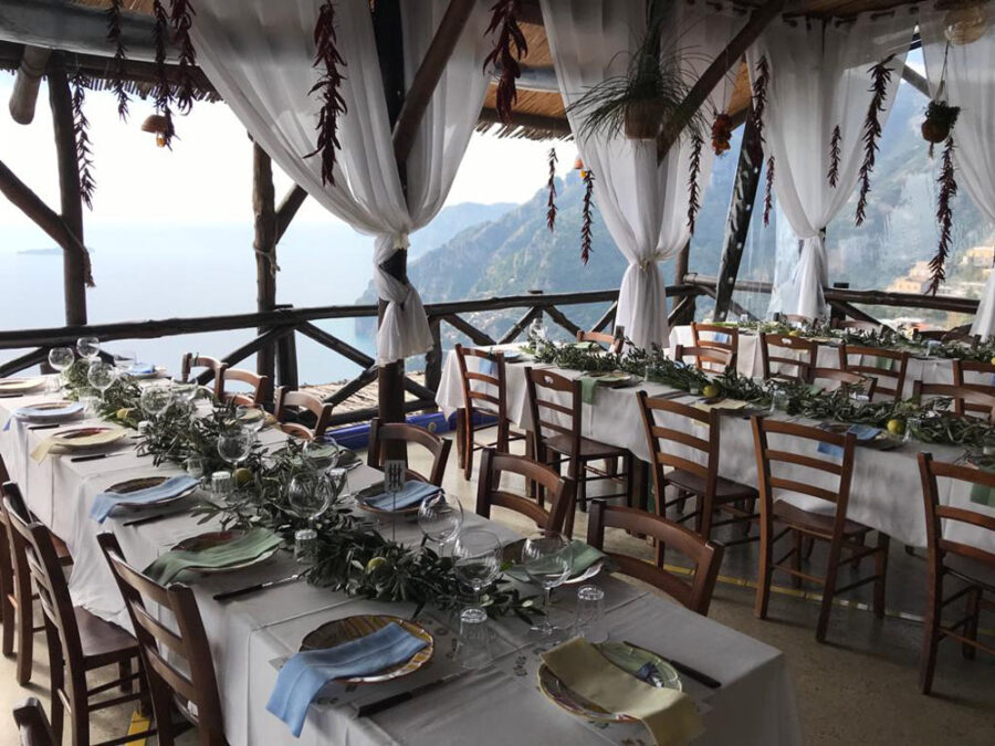 Cliffside Mediterranean banquet terrace with long communal tables and panoramic sea view.