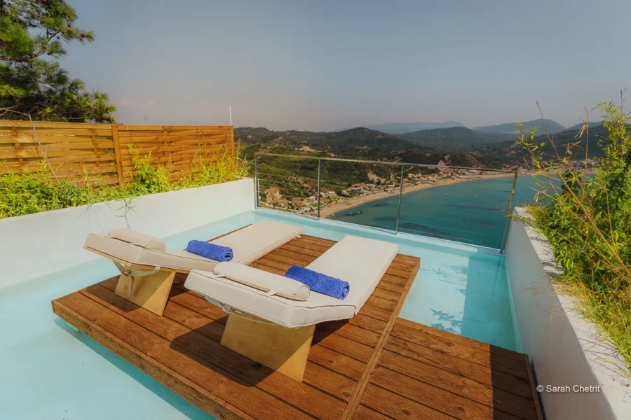 Luxurious seaside terrace with sun loungers, wooden deck, glass railing, and scenic coastal view.