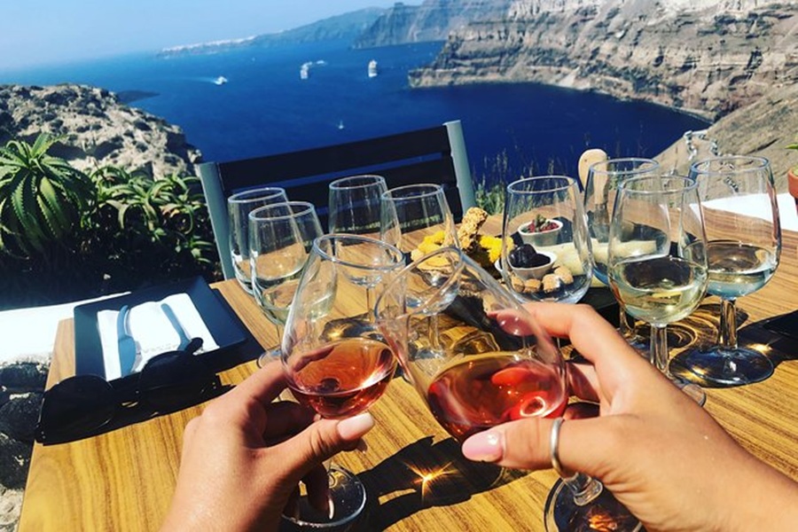 Toasting rosé wine in Santorini, overlooking Aegean Sea with desserts and cliffside views.