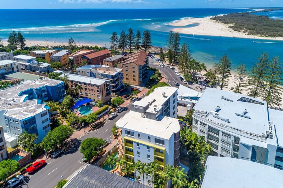 Aerial view of Bulcock Beach accommodation, coastal apartments, hotels, swimming pool, inlet and sandy shoreline.