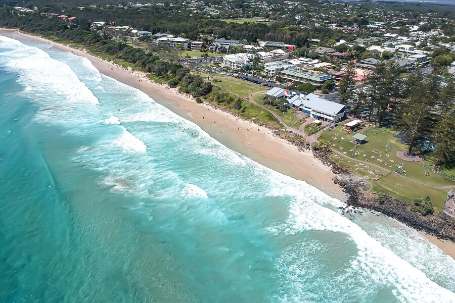 Aerial view of Byron Bay Australia beach, turquoise ocean waves, coastal town and beachfront park.