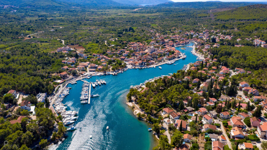 Aerial view of Vrboska: coastal town, Mediterranean architecture, lush hills, turquoise waterway.