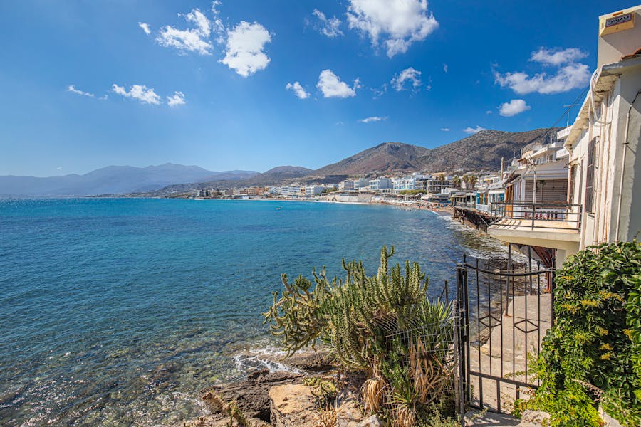 Mediterranean coastal town bay with turquoise sea, rocky shoreline, seaside houses, and mountains.