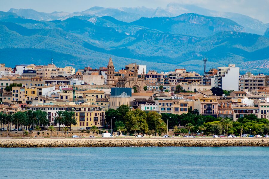 Palma de Mallorca coastal cityscape with cathedral, Mediterranean sea, palm-lined promenade and mountains.