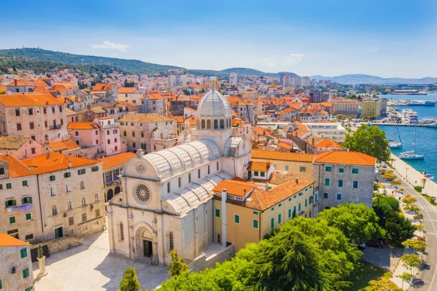Aerial view of historic coastal town with red roofs, church dome, and harbor in Croatia.