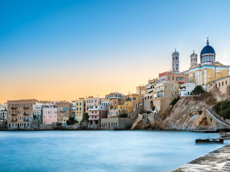Syros, Greece seaside town with blue-domed church and waterfront at sunset.