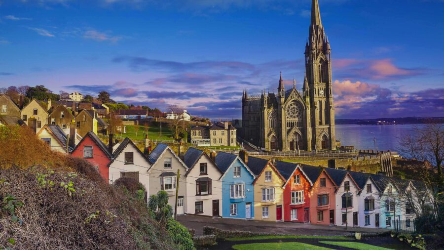 Colorful Cork, Ireland coastal houses and Gothic church spire overlooking the sea at sunset.